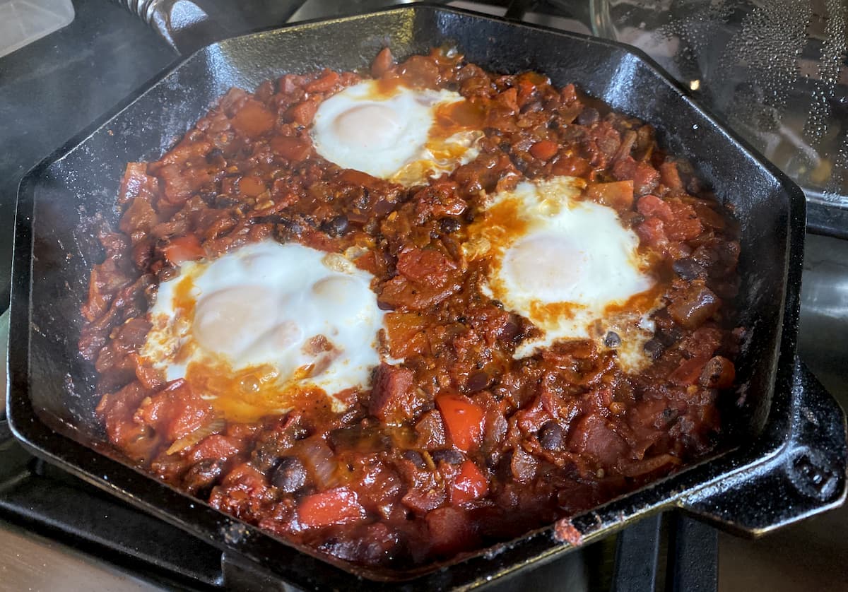 Mexican bean shakshuka with three eggs cooking in a cast iron pan