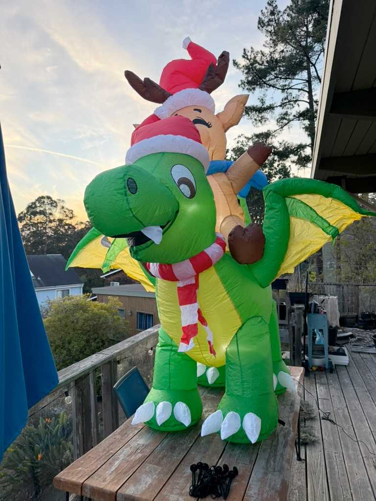 A large inflatable Christmas decoration of a reindeer riding a dragon - both reindeer and dragon are wearing Christmas hats