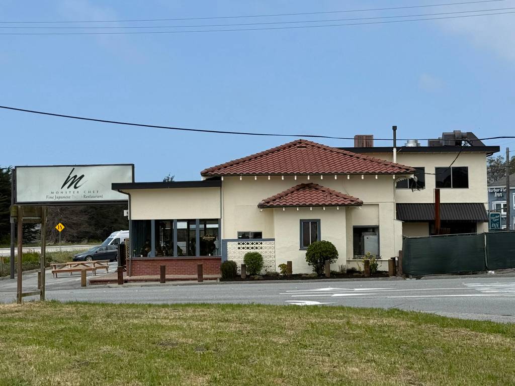 Exterior photo of a restaurant with a faded sign reading "MONSTER CHEF Fine Japanese Restaurant" the building is cream-colored with red tile roofs and large windows. It has a little bit of a railway station vibe to it if you squint at it just the right way.