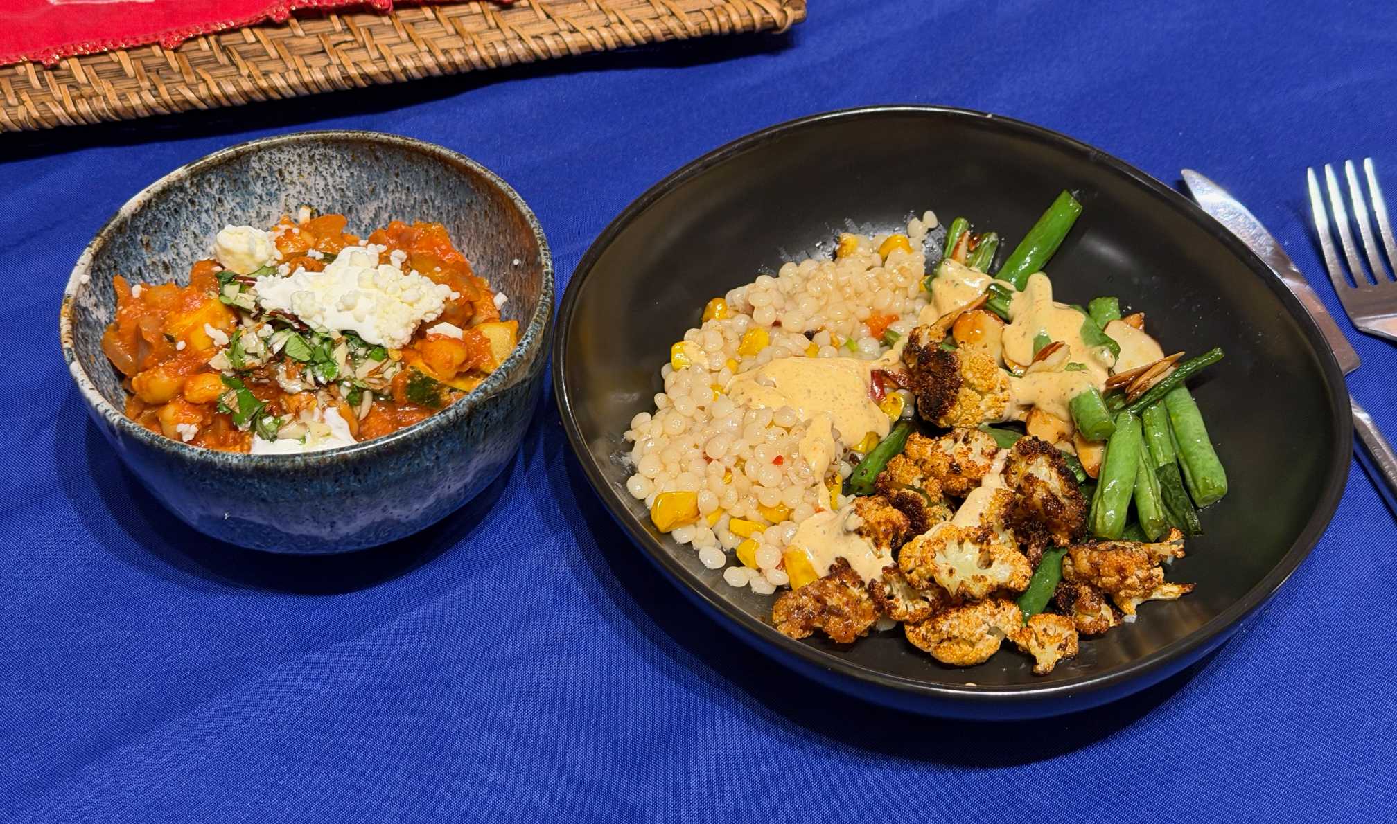 A small bowl (a beautiful blue sea textured bowl, made by Natalie Downe) contains a chickpea stew. A larger black bowl has couscous, green beans and blackened cauliflower.