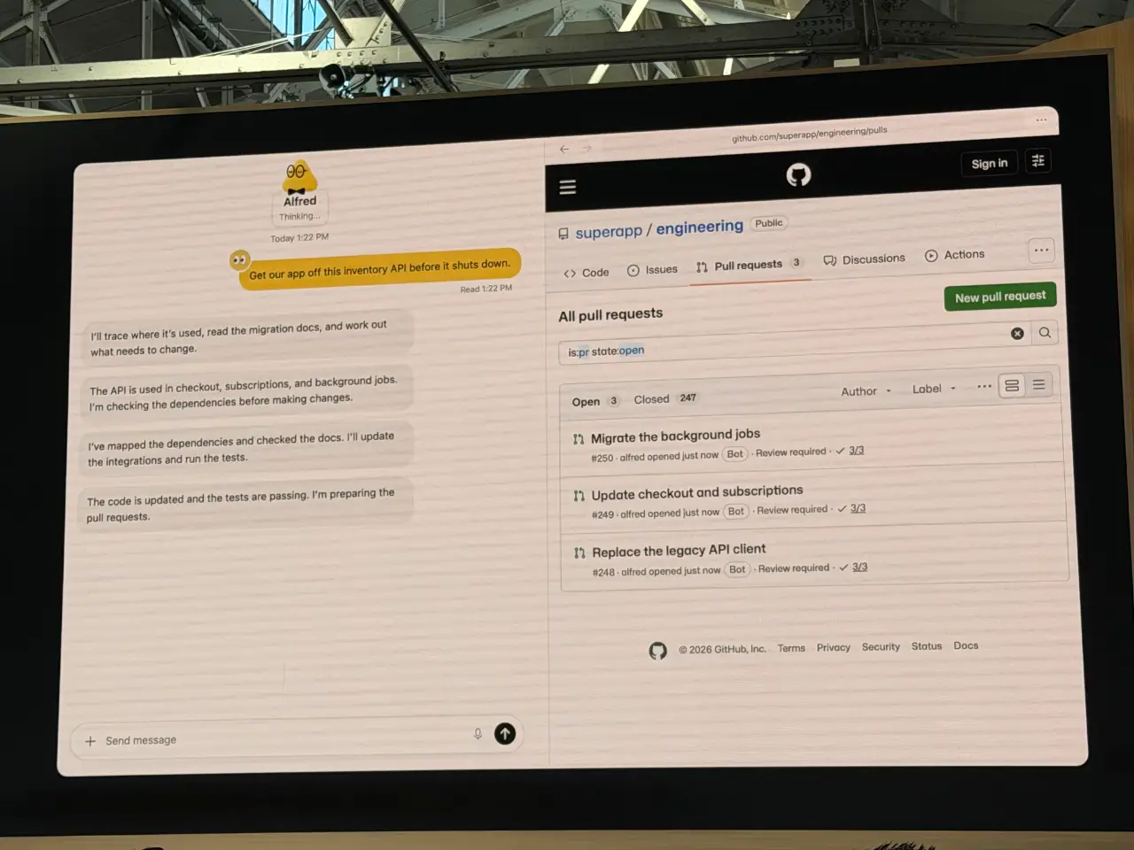 A large display in an industrial venue shows a chat with Alfred alongside a GitHub page for the public “superapp/engineering” repository. Alfred is asked to remove an inventory API before it shuts down, then reports tracing its uses, checking dependencies, updating integrations and passing tests; GitHub lists three open pull requests: “Migrate the background jobs,” “Update checkout and subscriptions,” and “Replace the legacy API client.”
