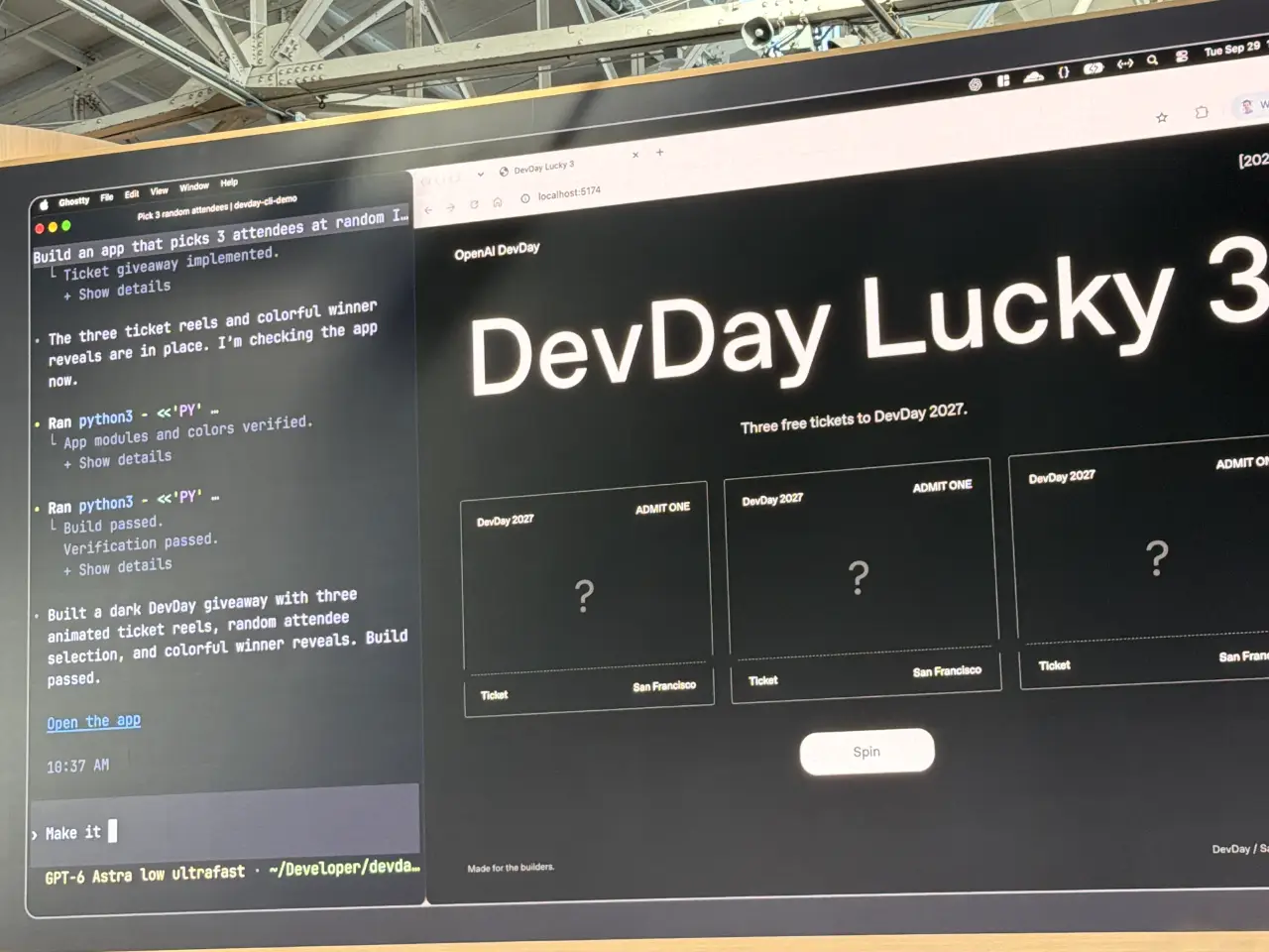 A large monitor at an OpenAI DevDay display shows a dark “DevDay Lucky 3” webpage offering three free tickets to DevDay 2027, with three ticket cards and a “Spin” button. A coding assistant panel beside it says the giveaway app is built and the build passed verification.